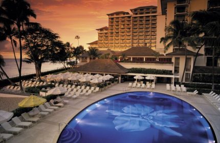 Halekulani Hotel pool at sunset. Gay-friendly hotel with ocean view, lounge chairs, and palm trees. Luxury travel for gay men in Honolulu.