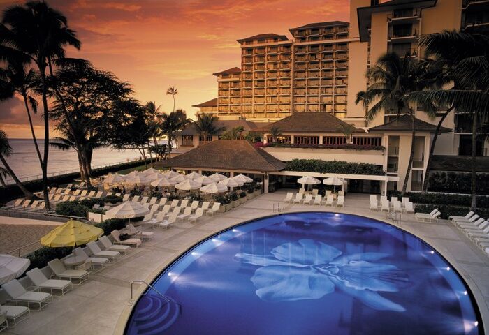 Halekulani Hotel pool at sunset. Gay-friendly hotel with ocean view, lounge chairs, and palm trees. Luxury travel for gay men in Honolulu.