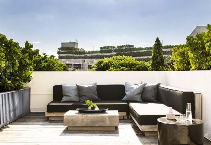 Kimpton Angler's Hotel gay-friendly space. Outdoor lounge area with a modern sofa, pillows, and tables. Lush greenery surrounds the rooftop patio.