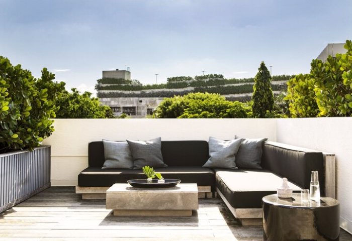 Kimpton Angler's Hotel gay-friendly space. Outdoor lounge area with a modern sofa, pillows, and tables. Lush greenery surrounds the rooftop patio.