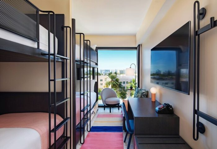 Moxy Miami South Beach gay-friendly hotel room. Bunk beds, desk, TV, & city view. Modern design, colorful rug. Ideal for gay travel in Miami.