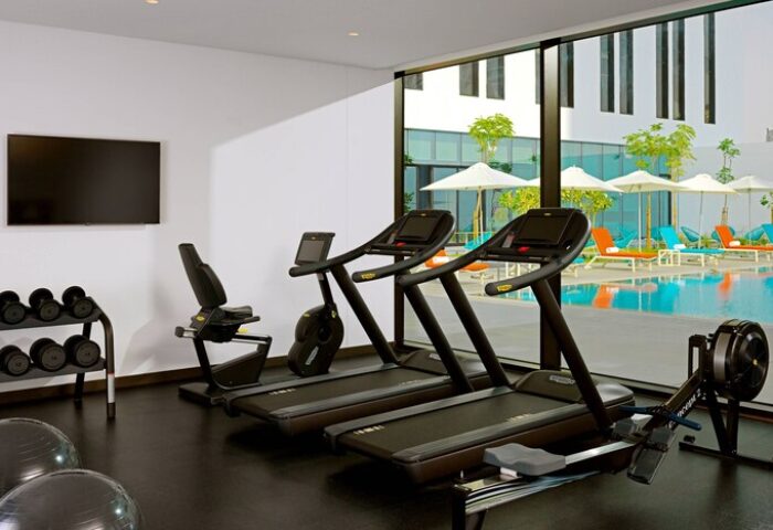 Aloft Me'aisam Dubai gym with treadmills, weights, bike, and rowing machine. Pool view. Gay-friendly hotel fitness center.