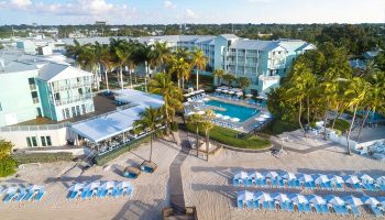 Aerial view of The Reach Key West, Curio Collection by Hilton, a gay-friendly hotel with a pool, beach, palm trees, and lounge chairs.
