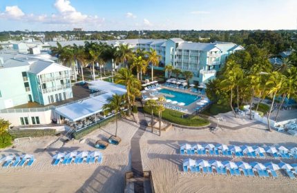Aerial view of The Reach Key West, Curio Collection by Hilton, a gay-friendly hotel with a pool, beach, palm trees, and lounge chairs.