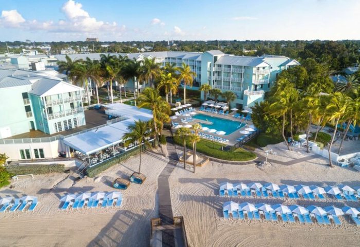 Aerial view of The Reach Key West, Curio Collection by Hilton, a gay-friendly hotel with a pool, beach, palm trees, and lounge chairs.