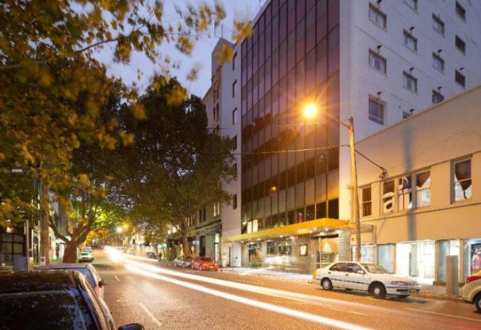 Exterior of 57 Hotel, a gay-friendly hotel. Street view with cars and city lights. Modern architecture and urban setting. Night scene.