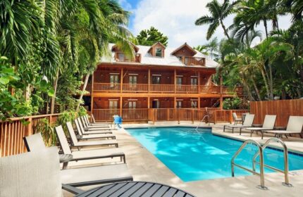 Island City House, a gay-friendly hotel. Poolside view of the wooden building with balconies, surrounded by palm trees, perfect for gay travel.