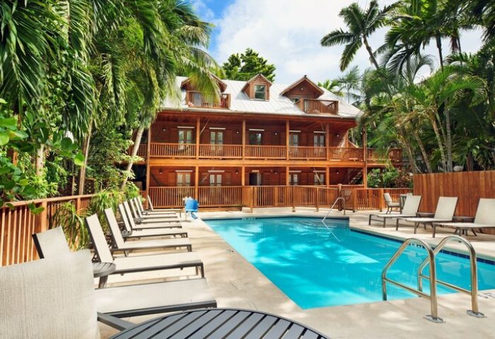 Island City House, a gay-friendly hotel. Poolside view of the wooden building with balconies, surrounded by palm trees, perfect for gay travel.