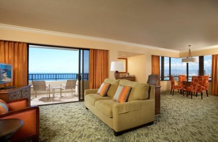 Hilton Hawaiian Village Waikiki Beach Resort gay-friendly hotel room. Ocean view from balcony, living area with sofa, dining table, and chairs.