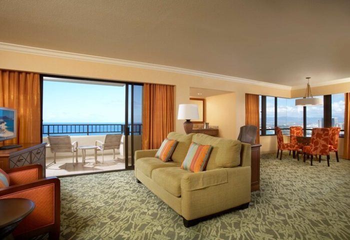 Hilton Hawaiian Village Waikiki Beach Resort gay-friendly hotel room. Ocean view from balcony, living area with sofa, dining table, and chairs.