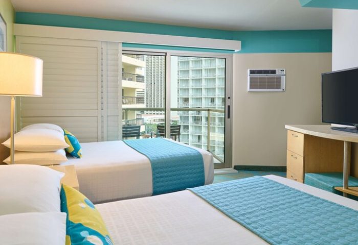 Aston Waikiki Circle Hotel room with two beds, balcony, and city view. Gay-friendly hotel for LGBTQ+ travelers. Modern design, comfortable stay.