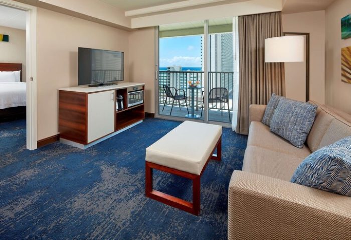 Hilton Garden Inn Waikiki Beach suite. Gay-friendly hotel with balcony ocean view, couch, TV, and bed. Modern room for gay travelers.