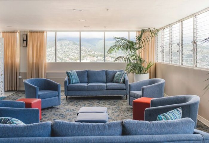 Pacific Monarch Hotel's gay-friendly room. Blue sofas and chairs arranged in a circle. Mountain view, plants, and modern decor.