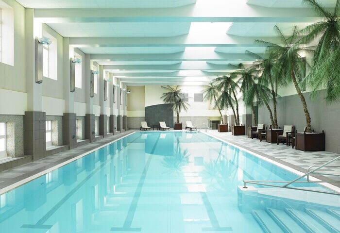 Indoor pool at London Marriott Hotel County Hall, a gay-friendly hotel. Palm trees line the pool, creating a relaxing, tropical vibe.