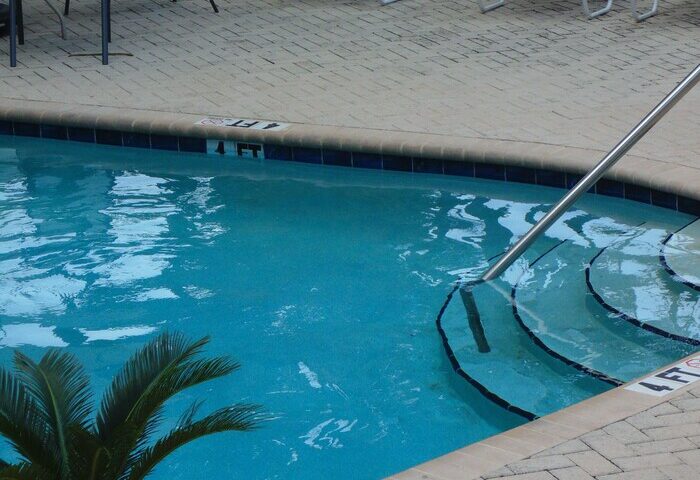 Cheston House gay-friendly hotel pool. Clothing optional all-male guesthouse with lounge chairs, palm tree, and inviting blue water.