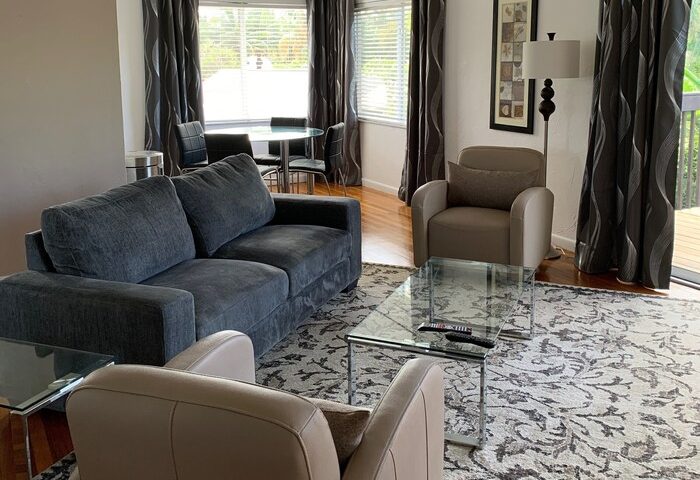 Living area at The Cabanas Guesthouse, a gay-friendly hotel. Features a sofa, armchairs, glass table, and dining set. Great for gay men's travel.