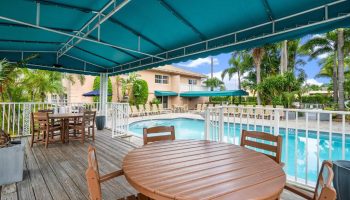 Coconut Bay Resort gay-friendly hotel pool view. Tables and chairs on a wooden deck, turquoise awning, palm trees, and lounge chairs.