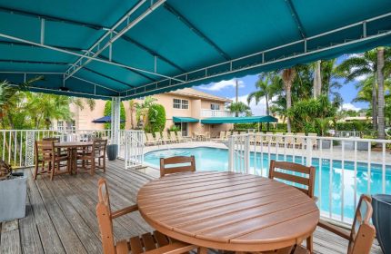 Coconut Bay Resort gay-friendly hotel pool view. Tables and chairs on a wooden deck, turquoise awning, palm trees, and lounge chairs.