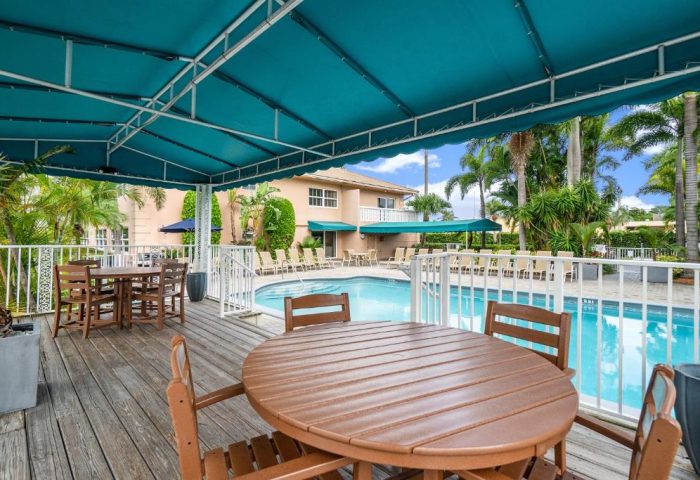 Coconut Bay Resort gay-friendly hotel pool view. Tables and chairs on a wooden deck, turquoise awning, palm trees, and lounge chairs.
