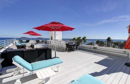 Gay-friendly hotel rooftop deck with red umbrellas, lounge chairs, and ocean view. Perfect for a relaxing vacation. Snooze at this gay hotel!