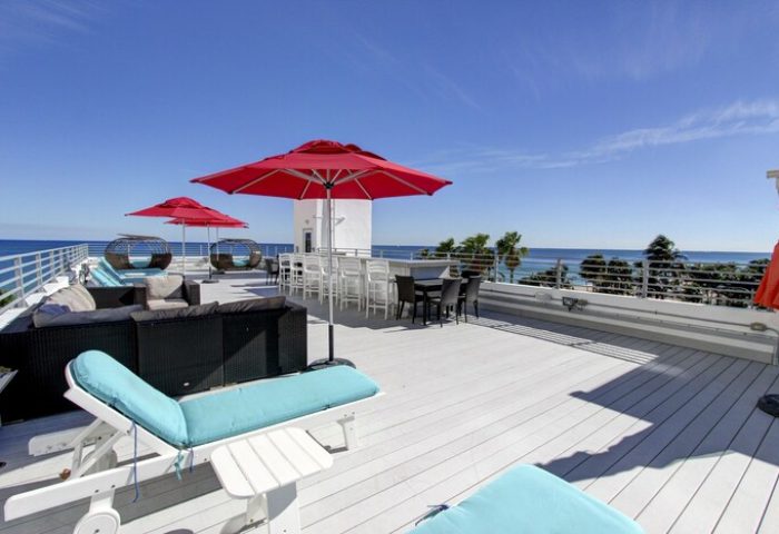 Gay-friendly hotel rooftop deck with red umbrellas, lounge chairs, and ocean view. Perfect for a relaxing vacation. Snooze at this gay hotel!