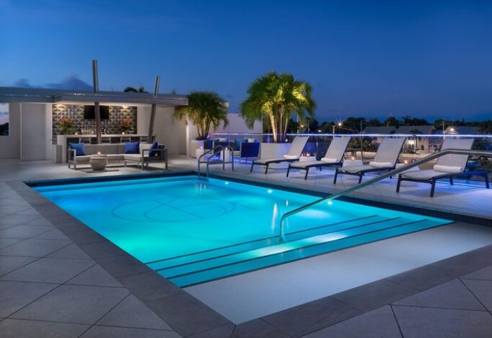 H2O Suites Adults Only gay-friendly hotel rooftop pool at night. Lounge chairs, bar, and palm trees create a relaxing atmosphere.