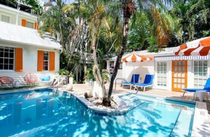 Marrero's Guest Mansion pool view. Gay-friendly hotel with lush tropical landscaping, white buildings, orange accents, and inviting blue pool.