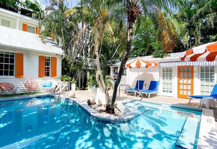 Marrero's Guest Mansion pool view. Gay-friendly hotel with lush tropical landscaping, white buildings, orange accents, and inviting blue pool.