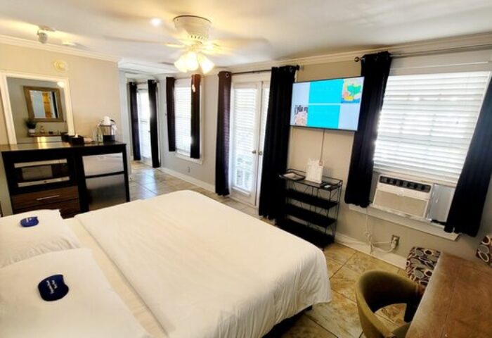Equator Resort's gay-friendly hotel room featuring a king-size bed with white linens, TV, air conditioning, and access to the balcony.