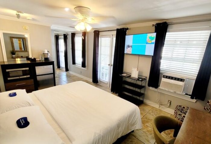 Equator Resort's gay-friendly hotel room featuring a king-size bed with white linens, TV, air conditioning, and access to the balcony.