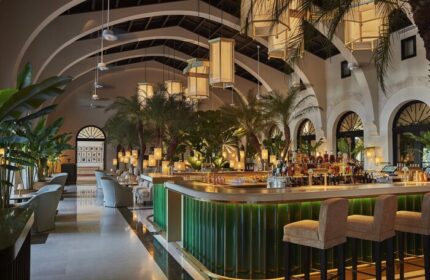 Interior of Four Seasons Hotel at The Surf Club, a gay-friendly hotel. Lush bar area with tropical plants and stylish seating. Upscale travel.