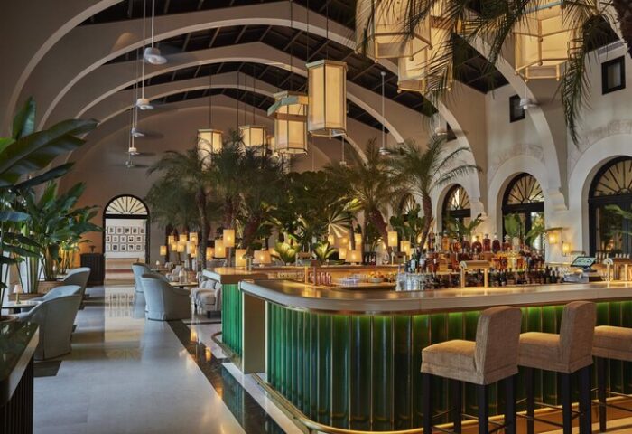 Interior of Four Seasons Hotel at The Surf Club, a gay-friendly hotel. Lush bar area with tropical plants and stylish seating. Upscale travel.