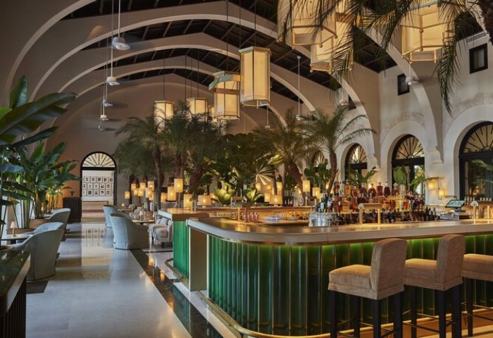 Interior of Four Seasons Hotel at The Surf Club, a gay-friendly hotel. Lush bar area with tropical plants and stylish seating. Upscale travel.