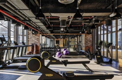 Gym at 25hours Hotel One Central, a gay-friendly hotel. Fitness equipment, treadmills, weights, and rowing machines. Modern design, brick wall.