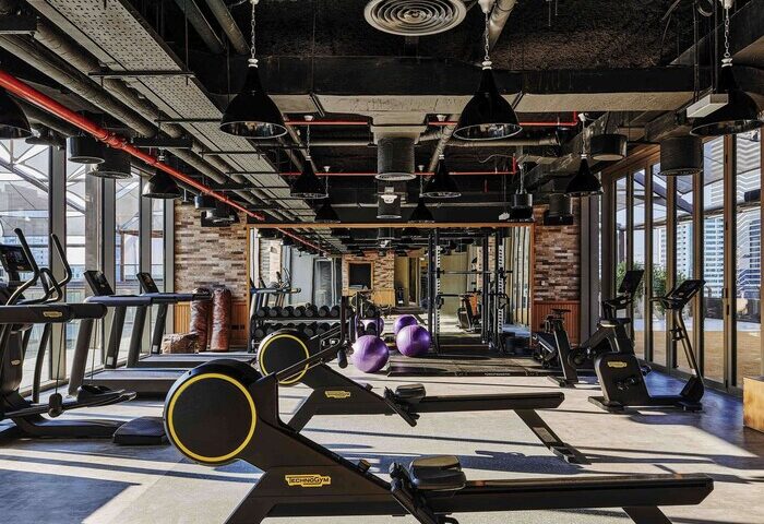 Gym at 25hours Hotel One Central, a gay-friendly hotel. Fitness equipment, treadmills, weights, and rowing machines. Modern design, brick wall.
