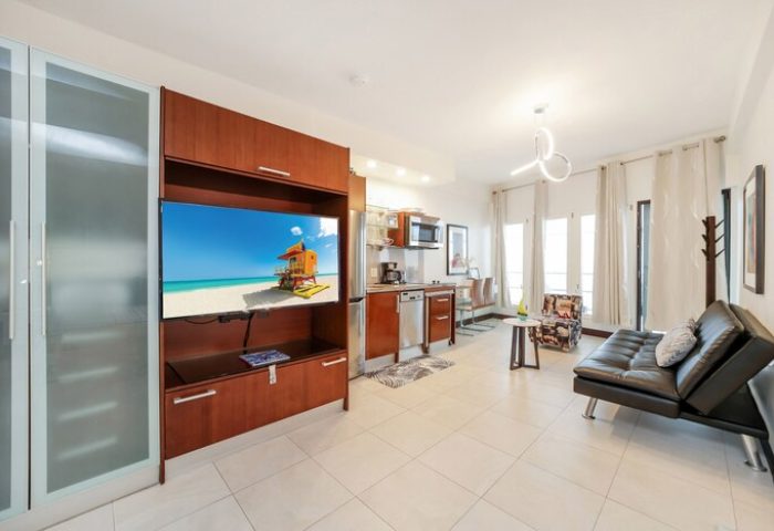 Ocean Drive Suites gay-friendly hotel room interior. Features a TV with a beach scene, kitchenette, and modern decor. Perfect for gay travel.
