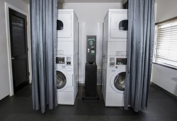 Laundry room at Posh South Beach, a gay-friendly hotel. Stacked washer and dryer units with a payment machine. Convenient amenities for gay travelers.