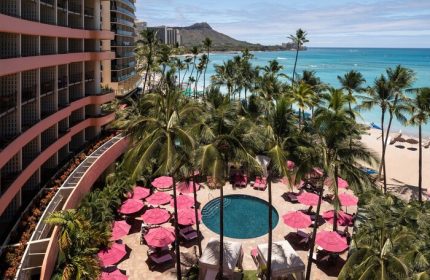 Royal Hawaiian, a Luxury Collection Resort, Waikiki pool view. Gay-friendly hotel with pink umbrellas, palm trees, and ocean backdrop.
