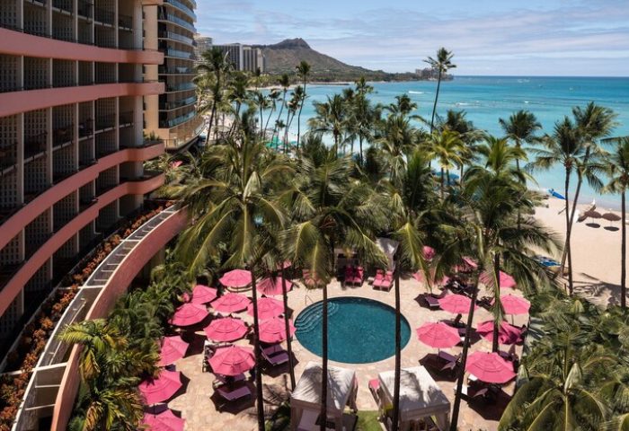 Royal Hawaiian, a Luxury Collection Resort, Waikiki pool view. Gay-friendly hotel with pink umbrellas, palm trees, and ocean backdrop.