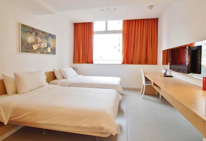 60 West Hotel's gay-friendly room. Two twin beds with white linens, orange curtains, desk, and TV. Modern design for gay travel.