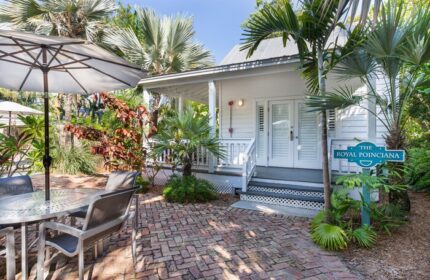 Paradise Inn adults only gay-friendly hotel exterior. Cottage with patio, table, umbrella, and tropical plants. The Royal Poinciana sign.