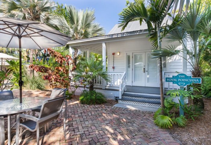 Paradise Inn adults only gay-friendly hotel exterior. Cottage with patio, table, umbrella, and tropical plants. The Royal Poinciana sign.