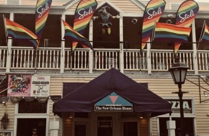 New Orleans House, a gay-friendly hotel. Rainbow flags and Stoli banners decorate the balcony. A jester figure stands above the entrance.