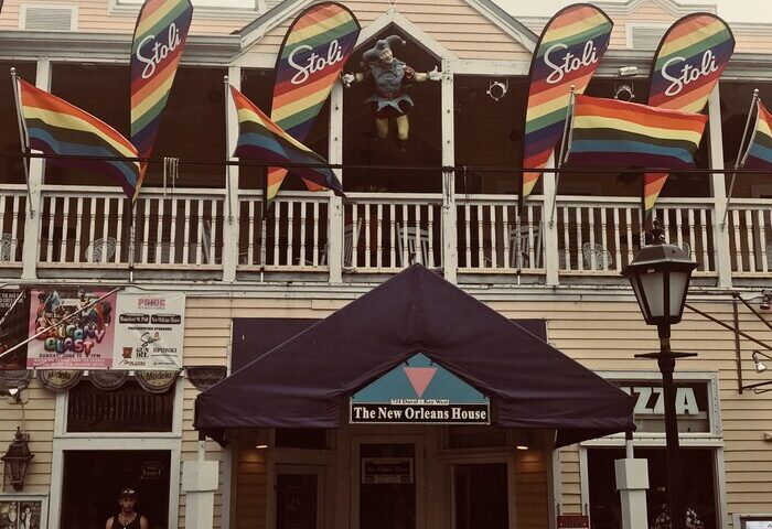 New Orleans House, a gay-friendly hotel. Rainbow flags and Stoli banners decorate the balcony. A jester figure stands above the entrance.