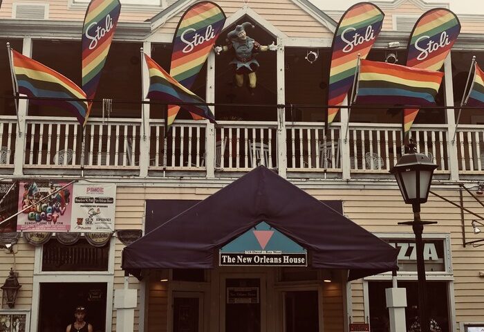 New Orleans House, a gay-friendly hotel. Rainbow flags and Stoli banners decorate the balcony. A jester figure stands above the entrance.