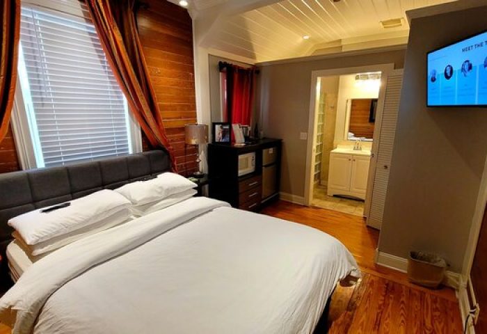 Equator Resort gay-friendly hotel room. Bed with white linens, wood walls, TV, and bathroom entrance. A comfortable stay for gay men travelers.