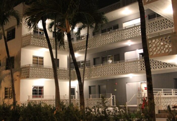 Hotel Gaythering, a gay-friendly hotel welcoming adults. Night view of the hotel's exterior with palm trees. Miami Beach gay travel.