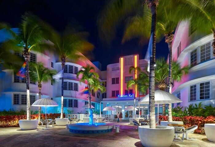 Axel Beach Miami gay-friendly hotel at night. Haddon Hall with neon lights, palm trees, fountain, and outdoor seating. Gay travel destination.