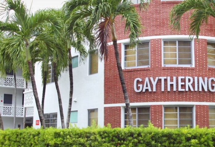 Gaythering: A gay-friendly hotel with palm trees. The building has a red brick section with the hotel's name and a white section.