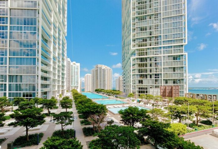 W Miami gay-friendly hotel view. Tall buildings, pools, and trees under a blue sky. A great place for gay men to travel and enjoy.
